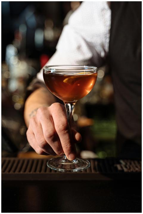 A bartender's hand holding a classy cocktail glass