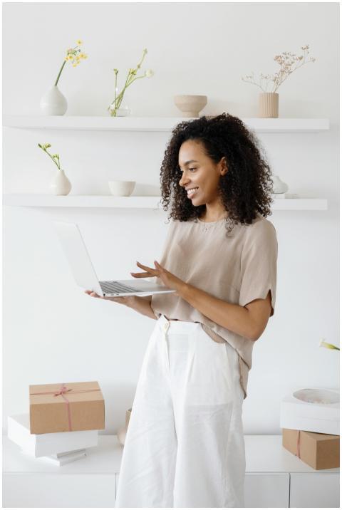 A smiling woman with curly hair works on a laptop
