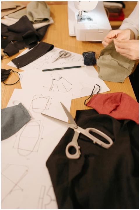Hands sewing face masks on a table with sewing too