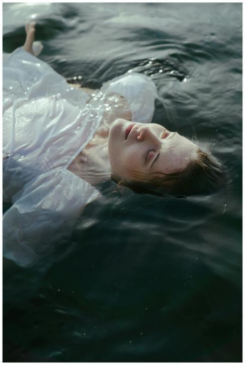 A serene woman in a white dress floats in a calm,