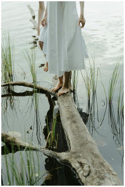 A barefoot woman in a white dress stands gracefull