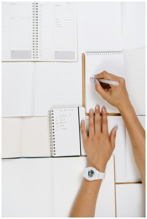 A person writing on a white notepad with a wristwa