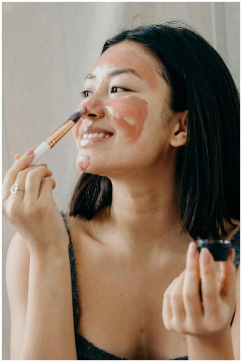Smiling woman applies clay mask using a brush, foc