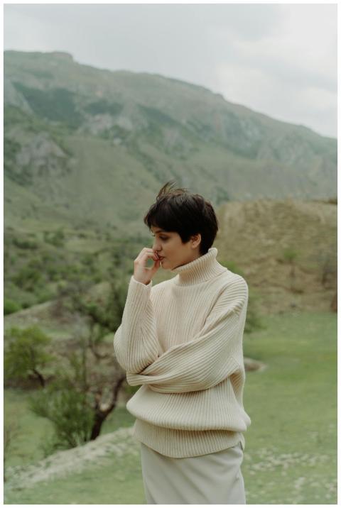 A woman in a cozy sweater stands thoughtfully agai