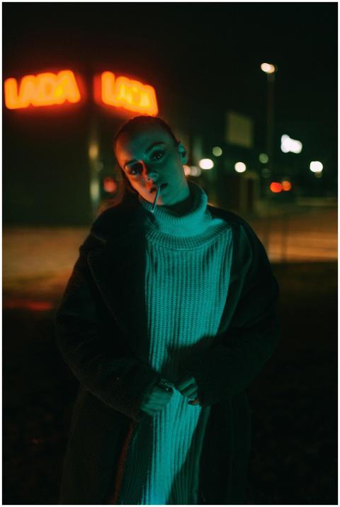 Fashionable woman poses at night with neon lights.