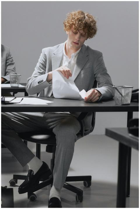 Man in gray suit tearing paper while seated at an