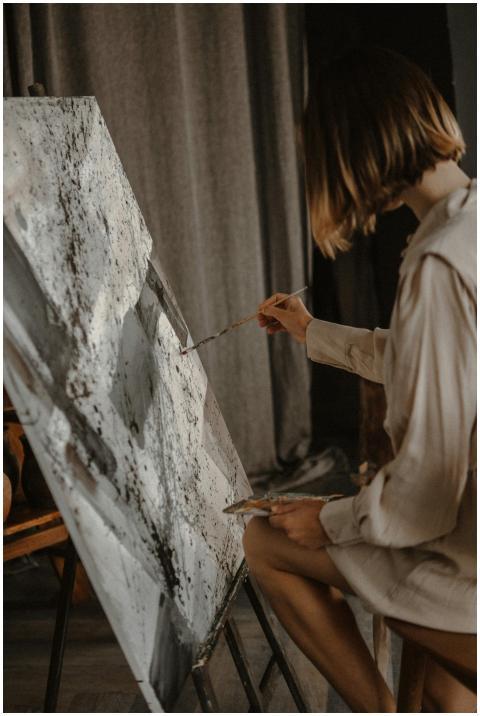 A focused artist painting on a canvas indoors, sho