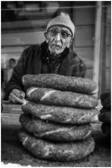 An elderly man in a bakery displays freshly baked