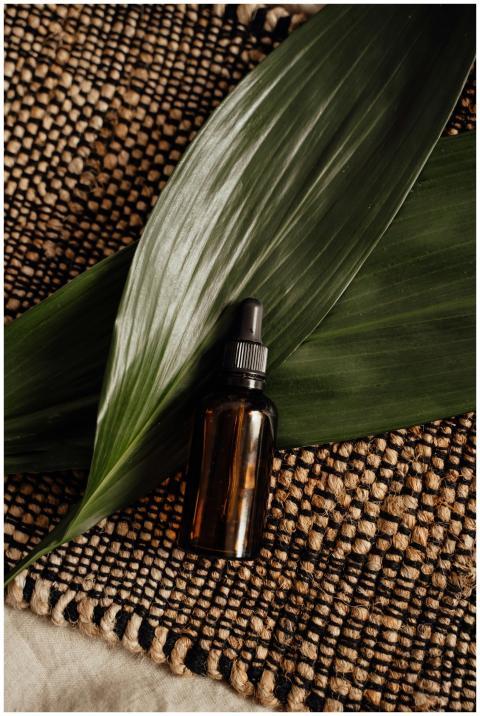 Brown glass dropper bottle on woven mat with green