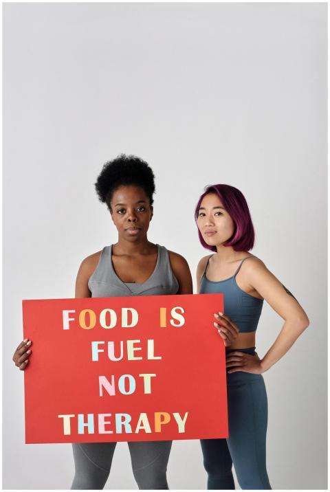 Two women stand confident with a sign promoting he