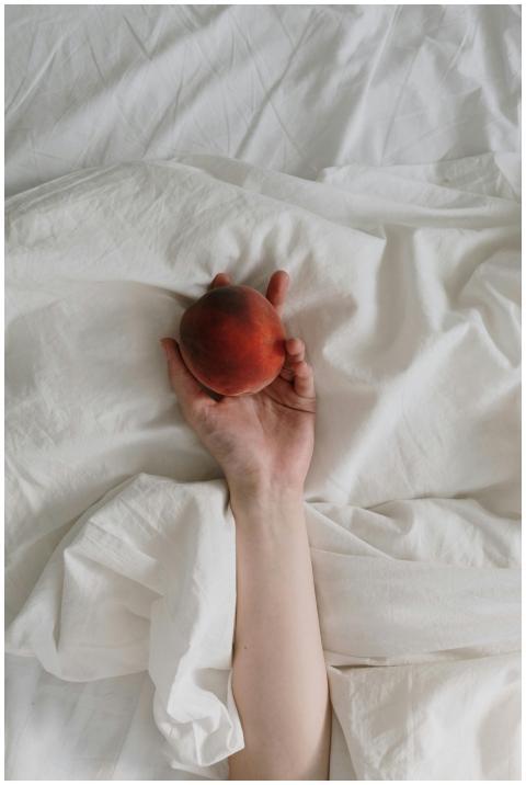 A person holds a peach in hand, resting on soft wh
