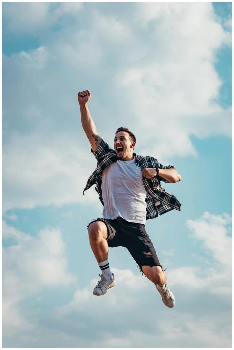 A joyful young man jumps midair with clouds and bl