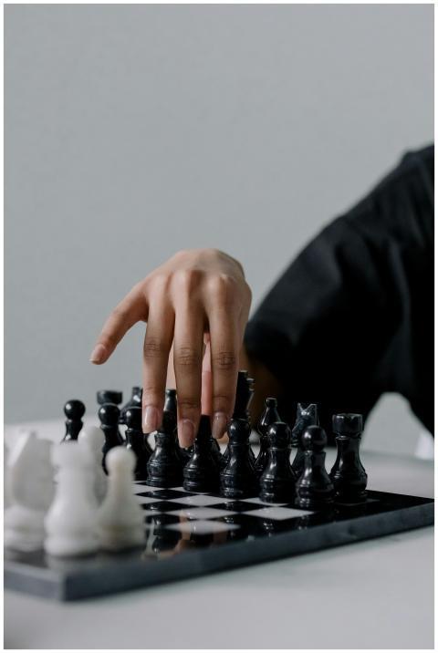 A hand moves a chess piece on a black and white ch
