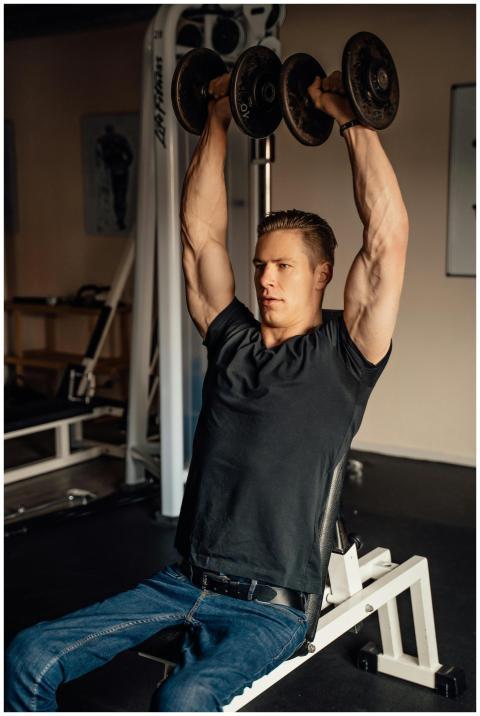 A muscular man lifting dumbbells while sitting ins