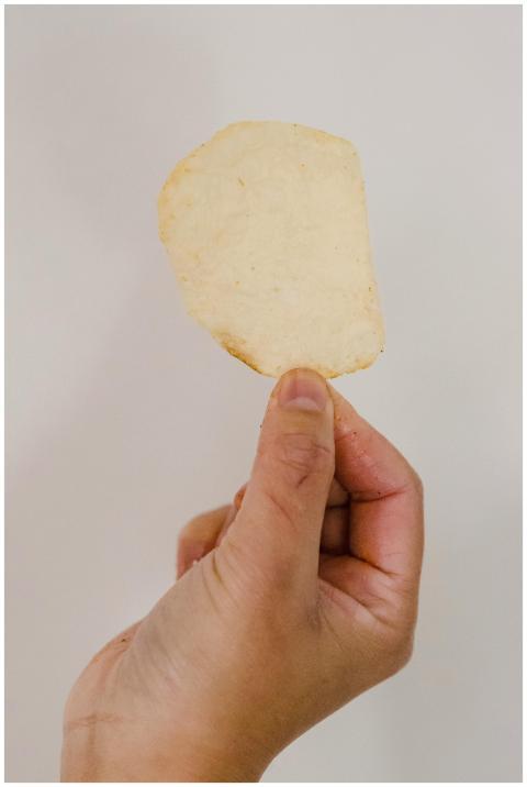 Close-up of a hand holding a single thin potato ch