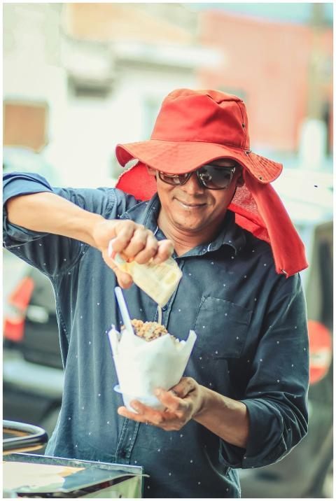 A man in a red hat serves street food with a smile