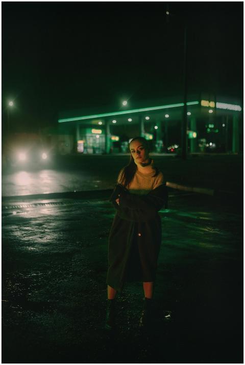 A woman stands confidently in front of a gas stati