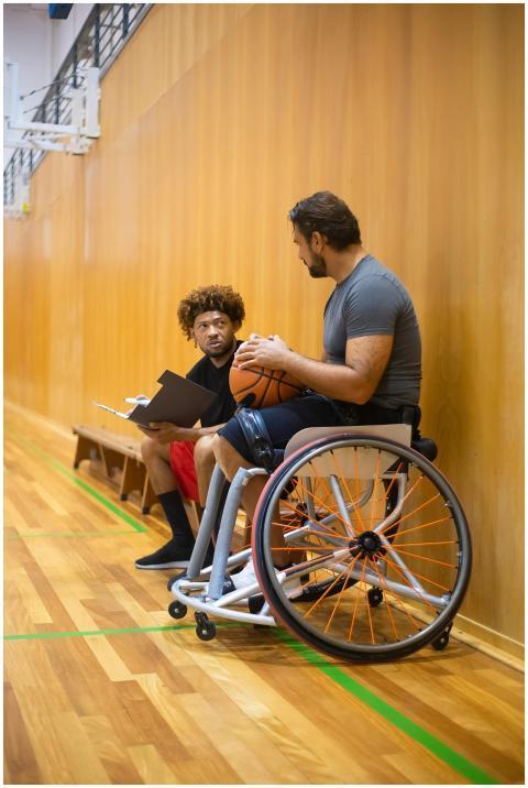 Man in wheelchair discussing with coach in a gym,