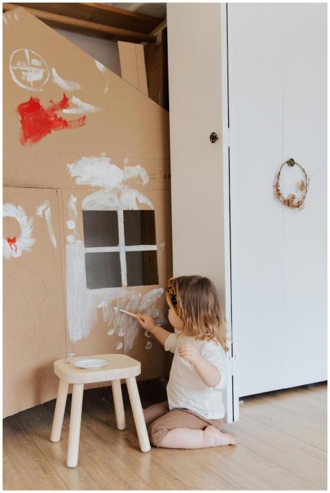 Little girl painting a cardboard house in a cozy i