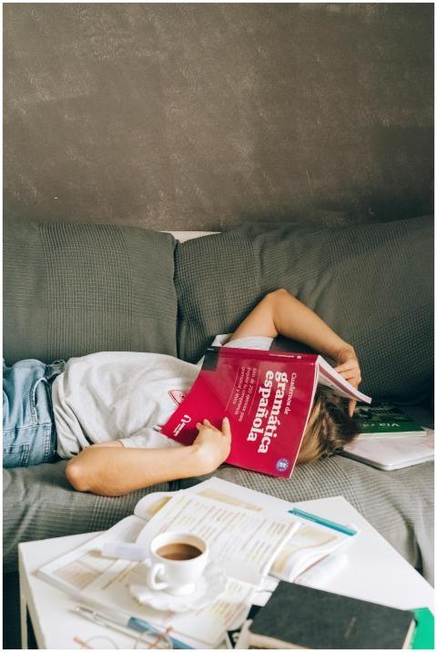 A tired student sleeps on a couch with a book cove