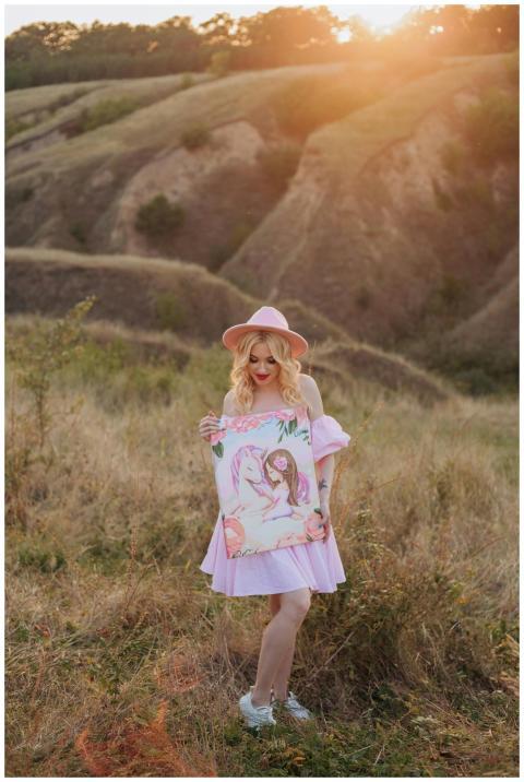 Blonde woman in pink dress displaying art in sceni