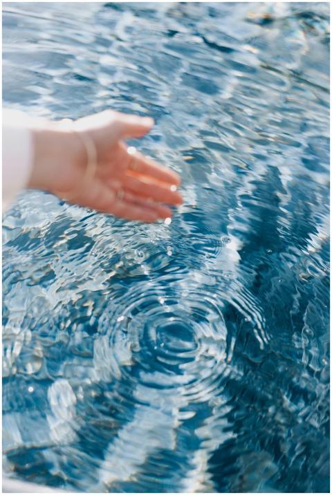 A close-up of a hand touching clear blue water cre