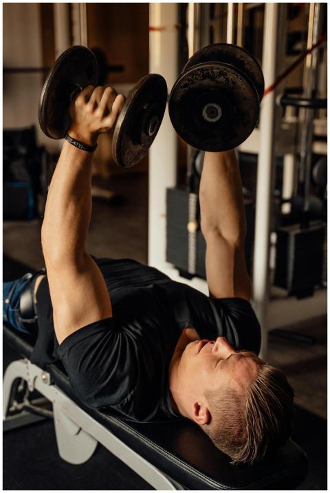 A muscular man lifting dumbbells while lying on a