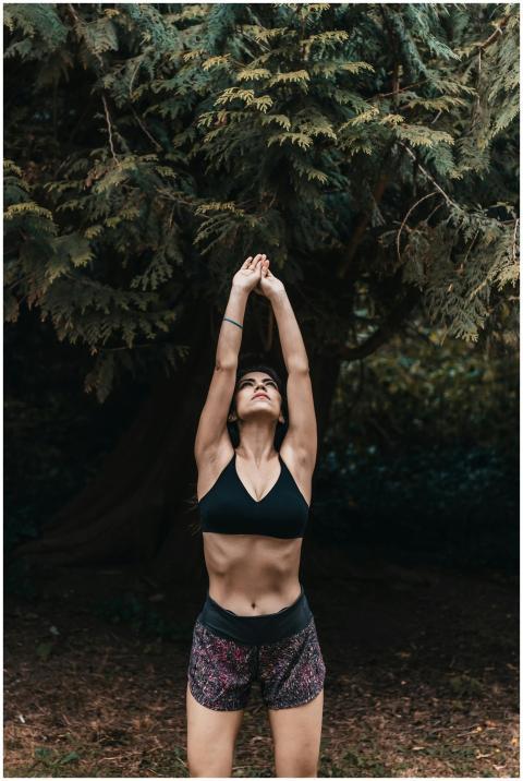 Woman in activewear stretching amidst greenery, em