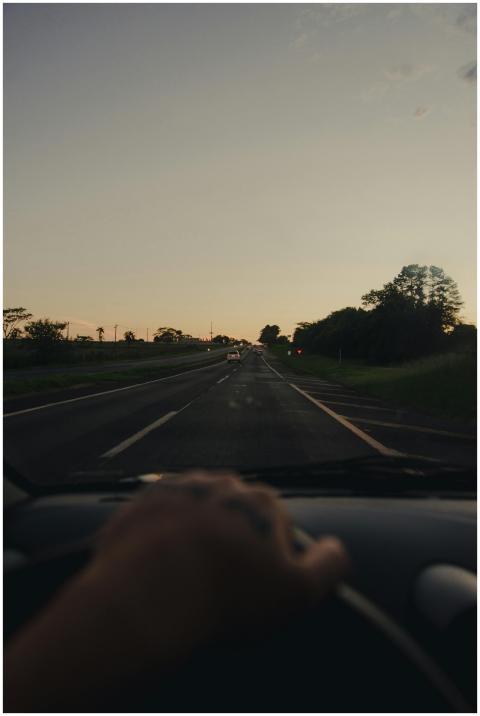 A hand on the steering wheel driving on a rural ro