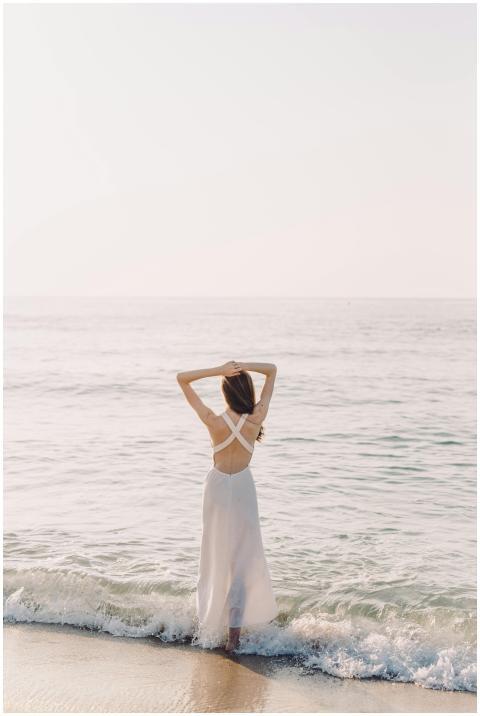 Woman stands on a serene beach at sunrise, embraci