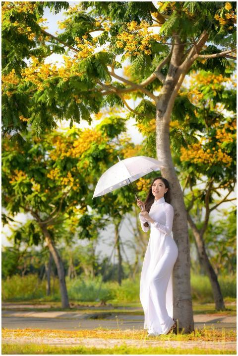 Asian woman in a white dress poses with an umbrell