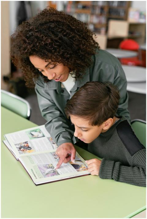 A teacher helps a student read a book at a green t