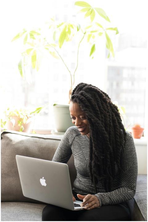 Black woman sitting on a sofa, smiling while worki