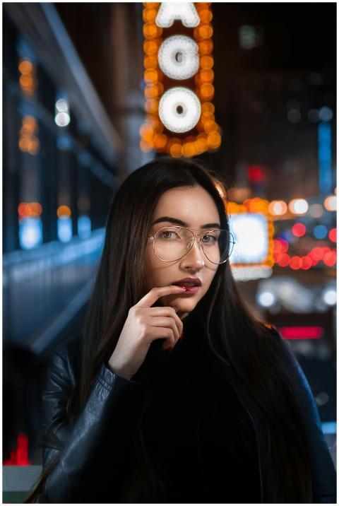 Young woman in glasses posing at night with city l