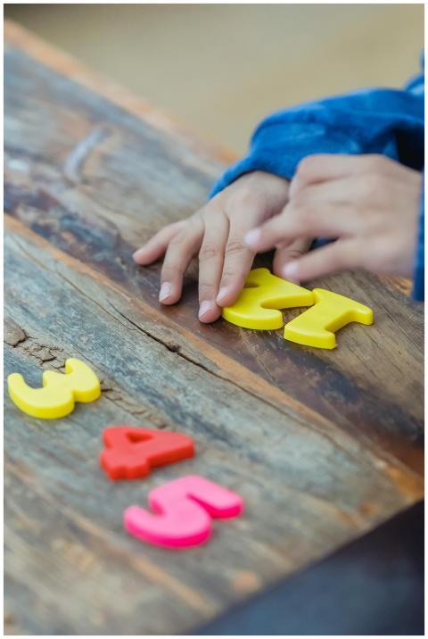 A child arranges colorful plastic numbers on a woo