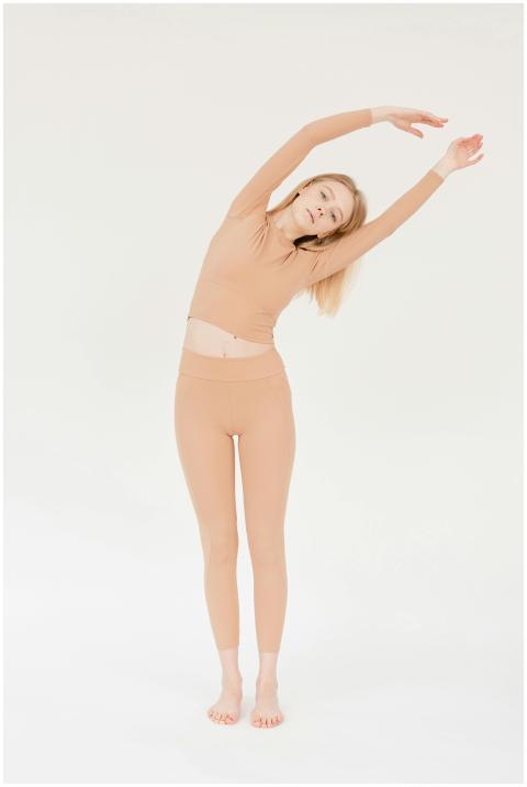 Young woman in beige activewear doing a yoga stret