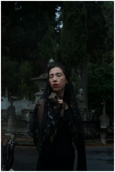 A woman in black stands solemnly in a dimly lit ce