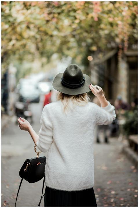 Fashionable woman in white sweater and hat strolli