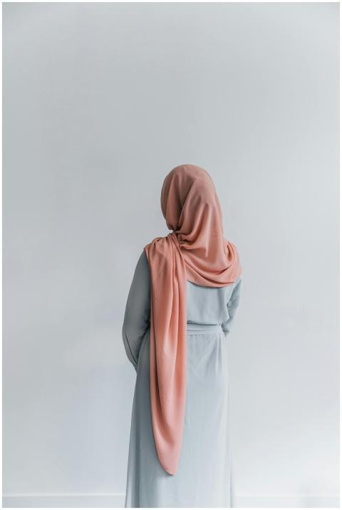 Elegant woman in a pink hijab standing against a s