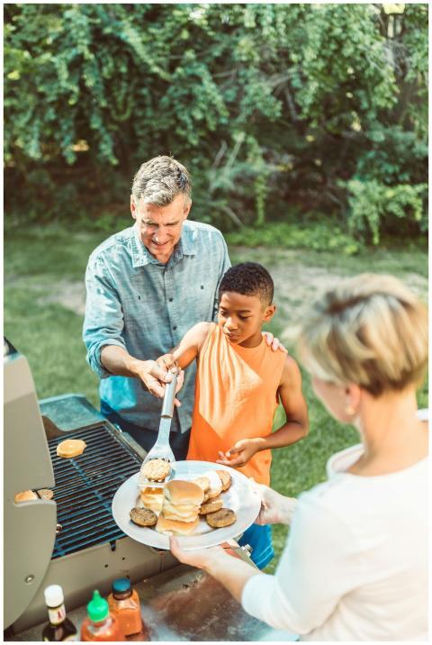 Father teaching son to grill burgers in a sunny ba