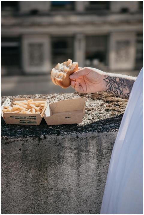 Hand holding a burger with fries in a box on a sun
