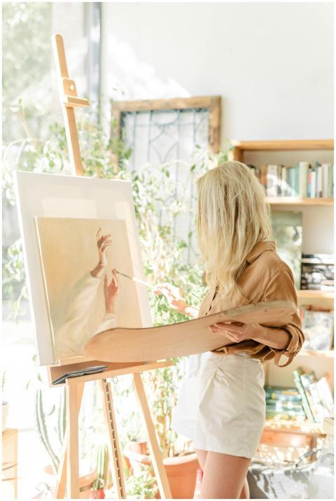 A blonde woman artist paints on canvas using oils
