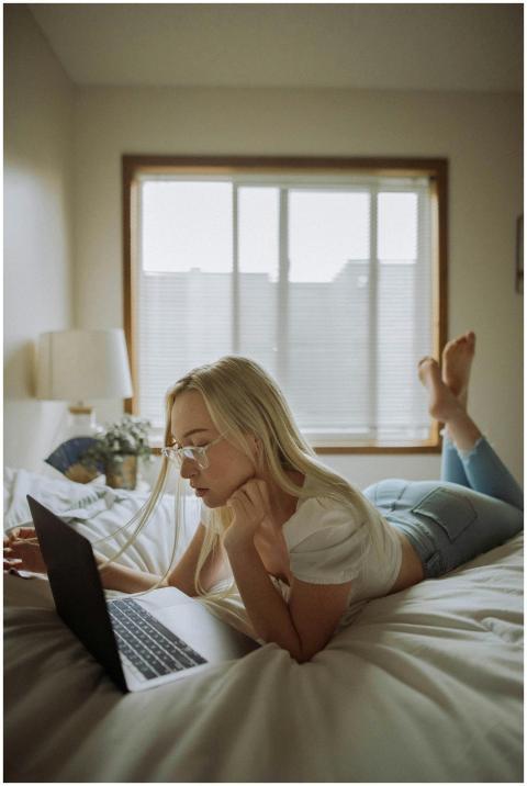 A woman in casual attire using a laptop while lyin
