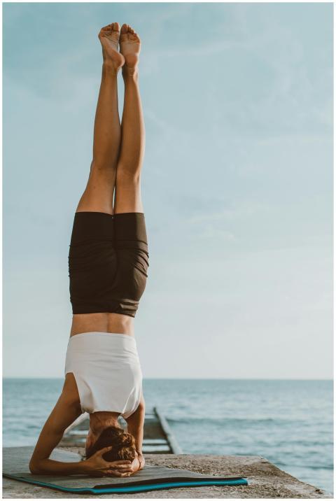 Woman performing a headstand on a dock by the ocea