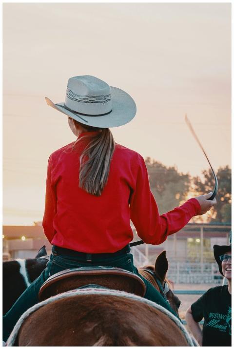 Back view of a cowgirl in a red shirt and cowboy h