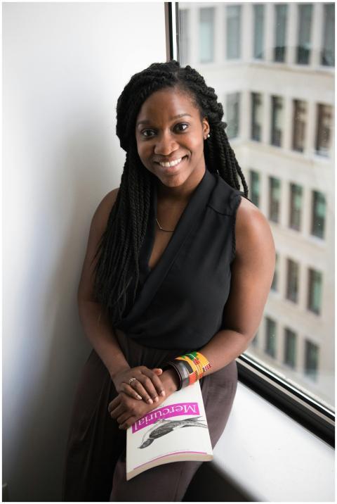 Confident young woman smiling with a book by the w