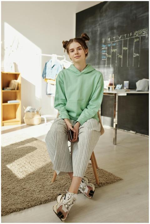 Teenage girl in a green hoodie sitting on a stool