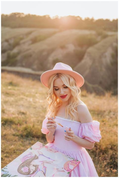 Blonde woman painting outdoors at sunset, wearing