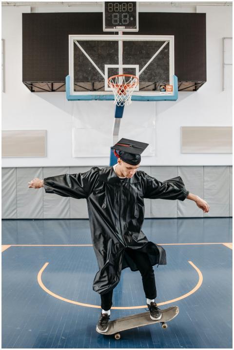 Young graduate in cap and gown skateboards in a gy