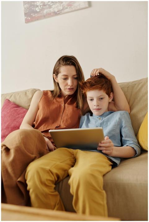 A mother and her son sitting on a couch, using a t